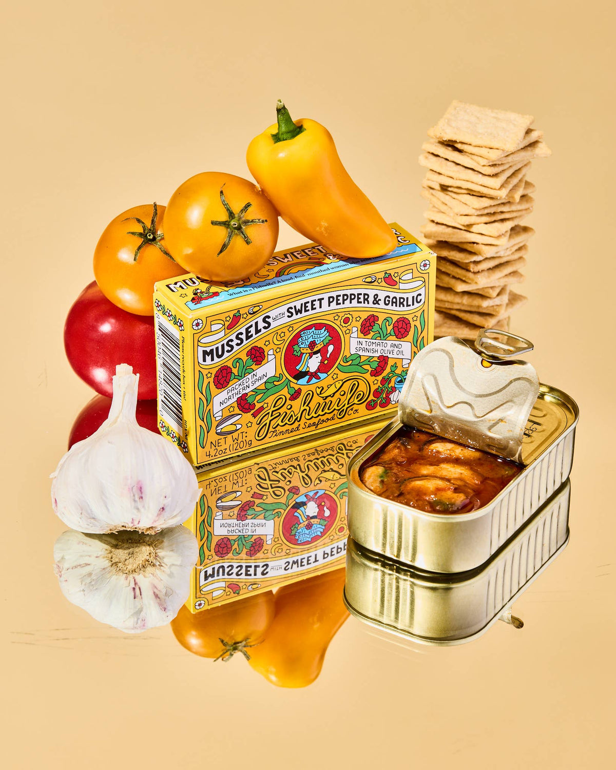 Tin of mussels with a decorative box, tomatoes, garlic, and crackers on a beige background
