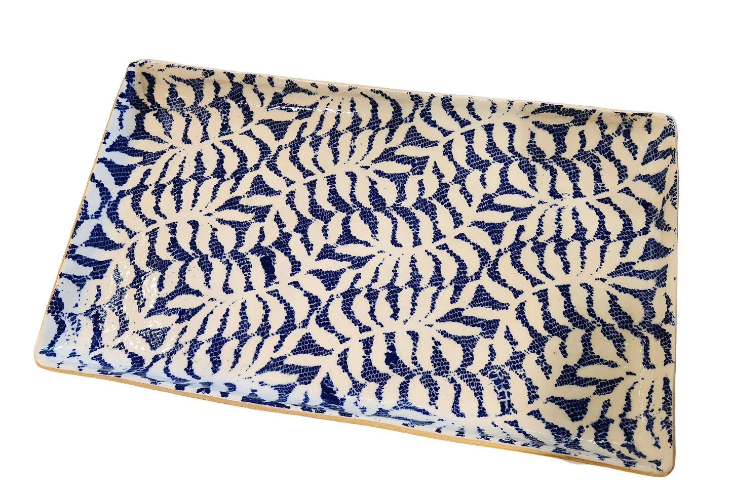 A rectangular ceramic serving platter with a navy blue and cream leaf pattern, shown on a rustic wooden floor.