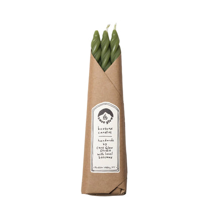 Three green candles in a brown paper sleeve with a label on a white background