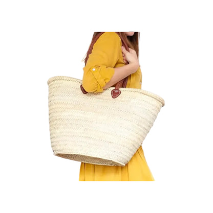 Person wearing a yellow outfit holding a large straw bag with a heart emblem on a white background