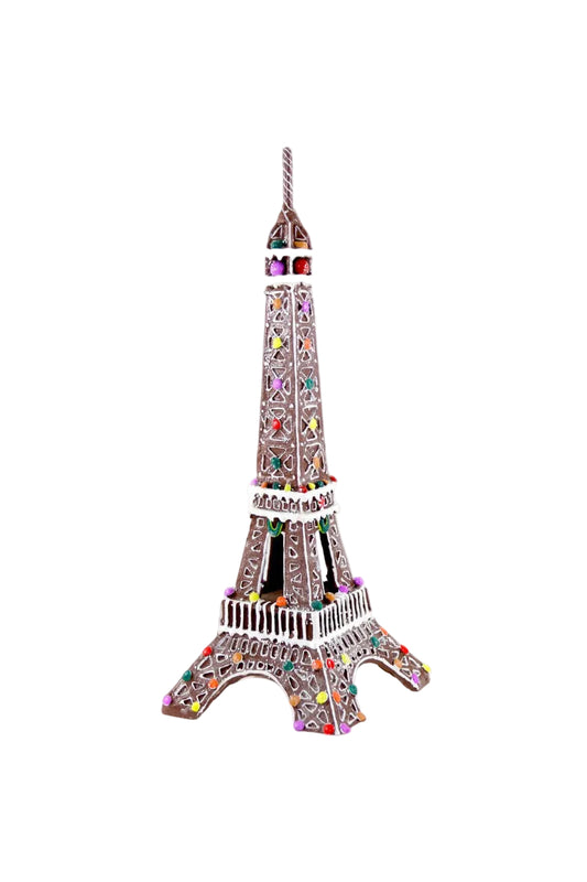 A decorative Eiffel Tower model made of brown icing with white icing outlines and colorful candy embellishments, photographed on a clean white background.