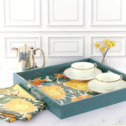 Teal tray with floral design holding teacups and saucers, set against a white cabinet background.