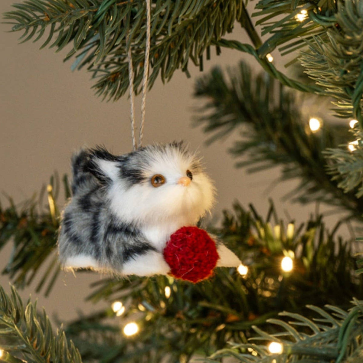 A small plush small kitten ornament with gray, white, and black fur hanging from a string o