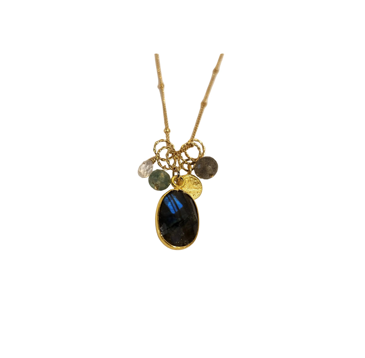 A gold chain necklace with a cluster of charms, featuring a large oval black labradorite stone pendant, a small gold coin charm, a clear crystal bead, a green stone bead, and a dark gray stone bead, displayed on a light beige background.