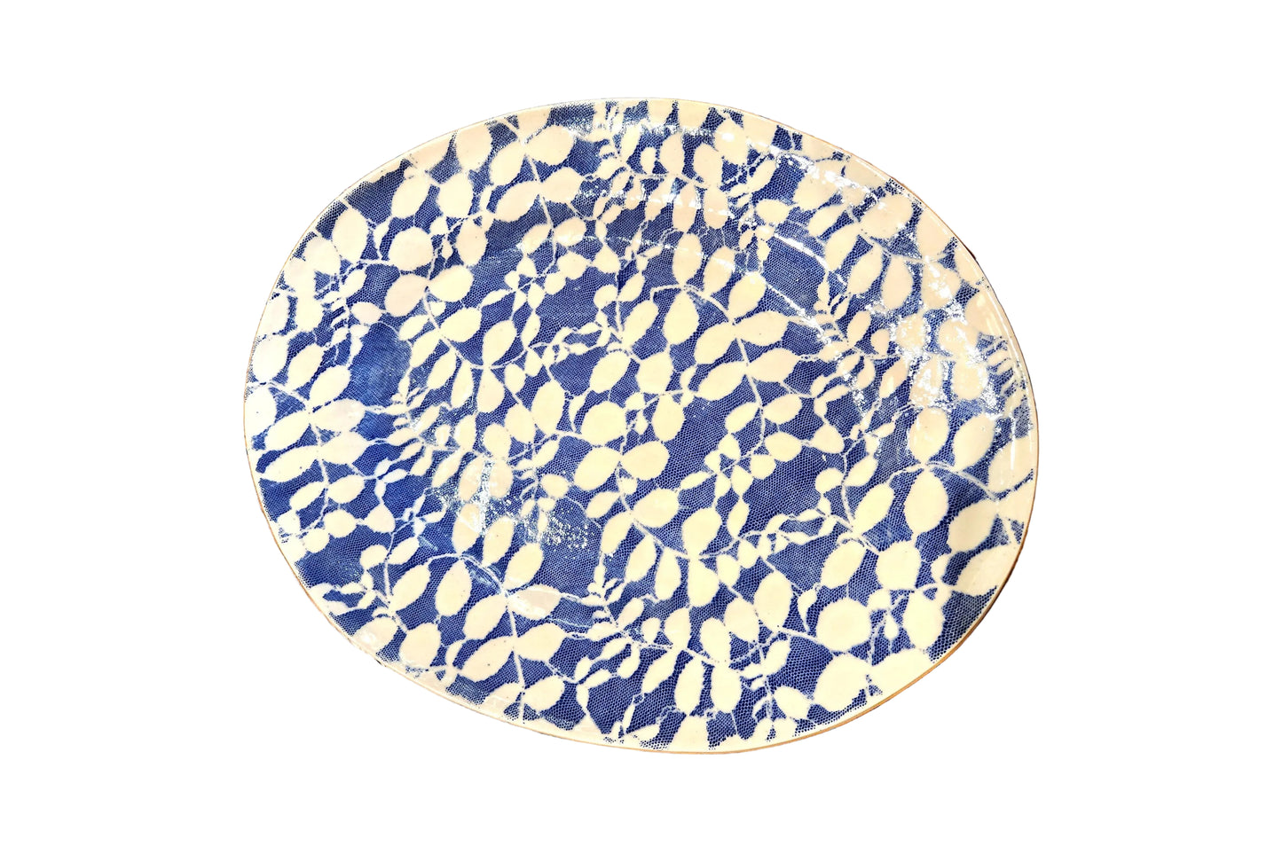 An oval ceramic plate with a blue and cream leaf pattern, photographed from above on a rustic wooden table.