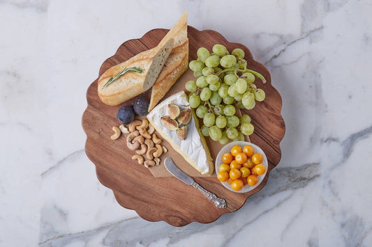 Wooden charcuterie board with bread, cheese, fruits, and nuts on a marble surface