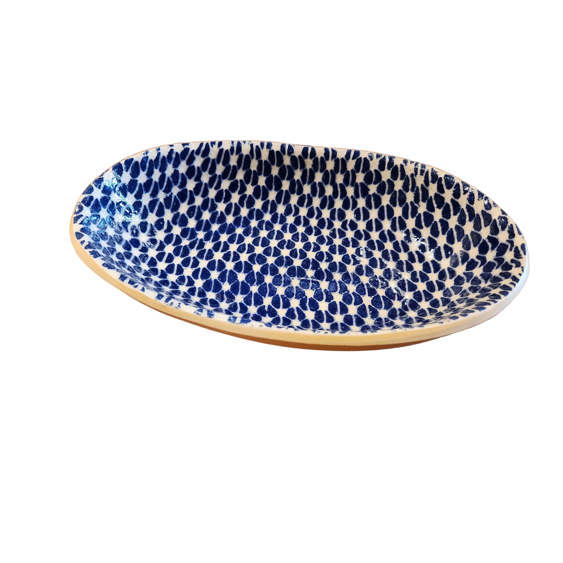 An oval ceramic dish with a blue and white spotted pattern and a natural unglazed beige rim, displayed on a rustic wooden table.