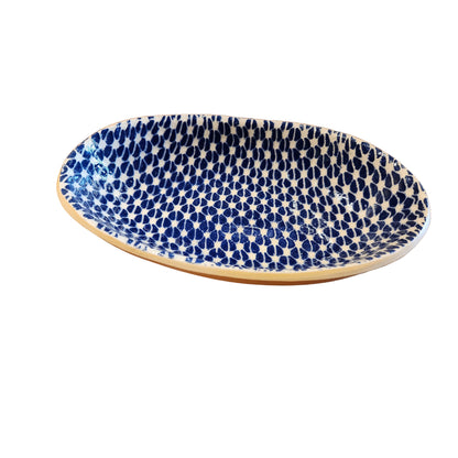 An oval ceramic dish with a blue and white spotted pattern and a natural unglazed beige rim, displayed on a rustic wooden table.