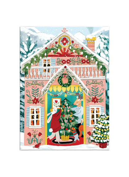 A colorful folk-art style illustration of a snow-covered pink house decorated for Christmas, with a wreath, garlands, windows, and a festive doorway where a rabbit and a cat are decorating a Christmas tree.