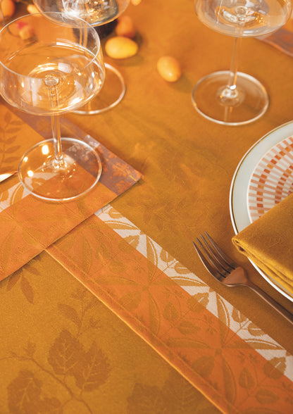 An orange damask tablecloth with a matching runner, styled with white plates, gold napkins, and clear wine glasses.
