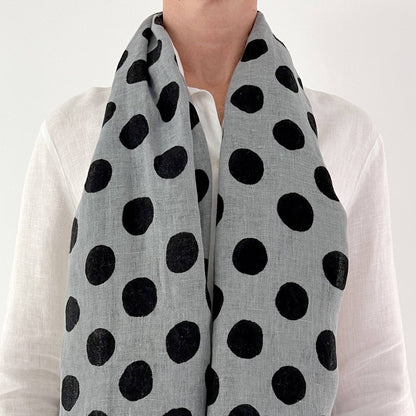Person wearing a gray scarf with black polka dots over a white shirt.