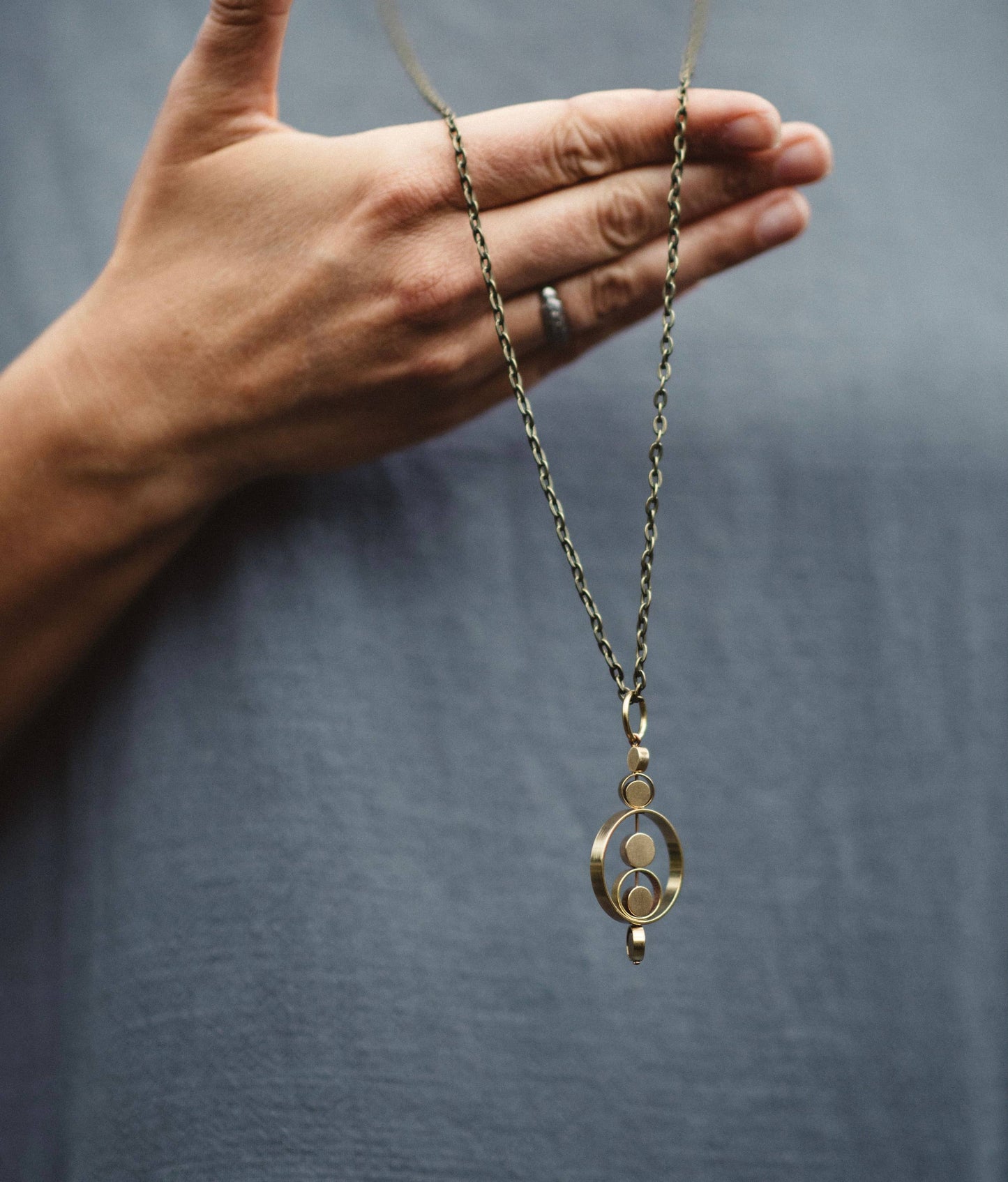 Hand holding a gold necklace with a pendant against a gray background