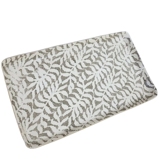 A rectangular cushion or pillow with a repeating leaf pattern in gray on an off-white background, shown against a solid light blue background.