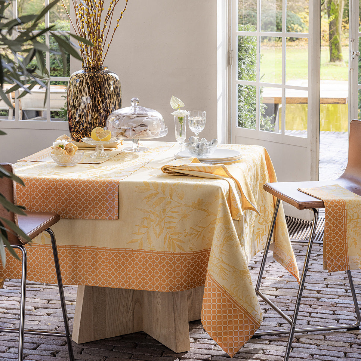 A set table featuring a yellow floral patterned tablecloth, with matching napkins and placemats, on a patio table.