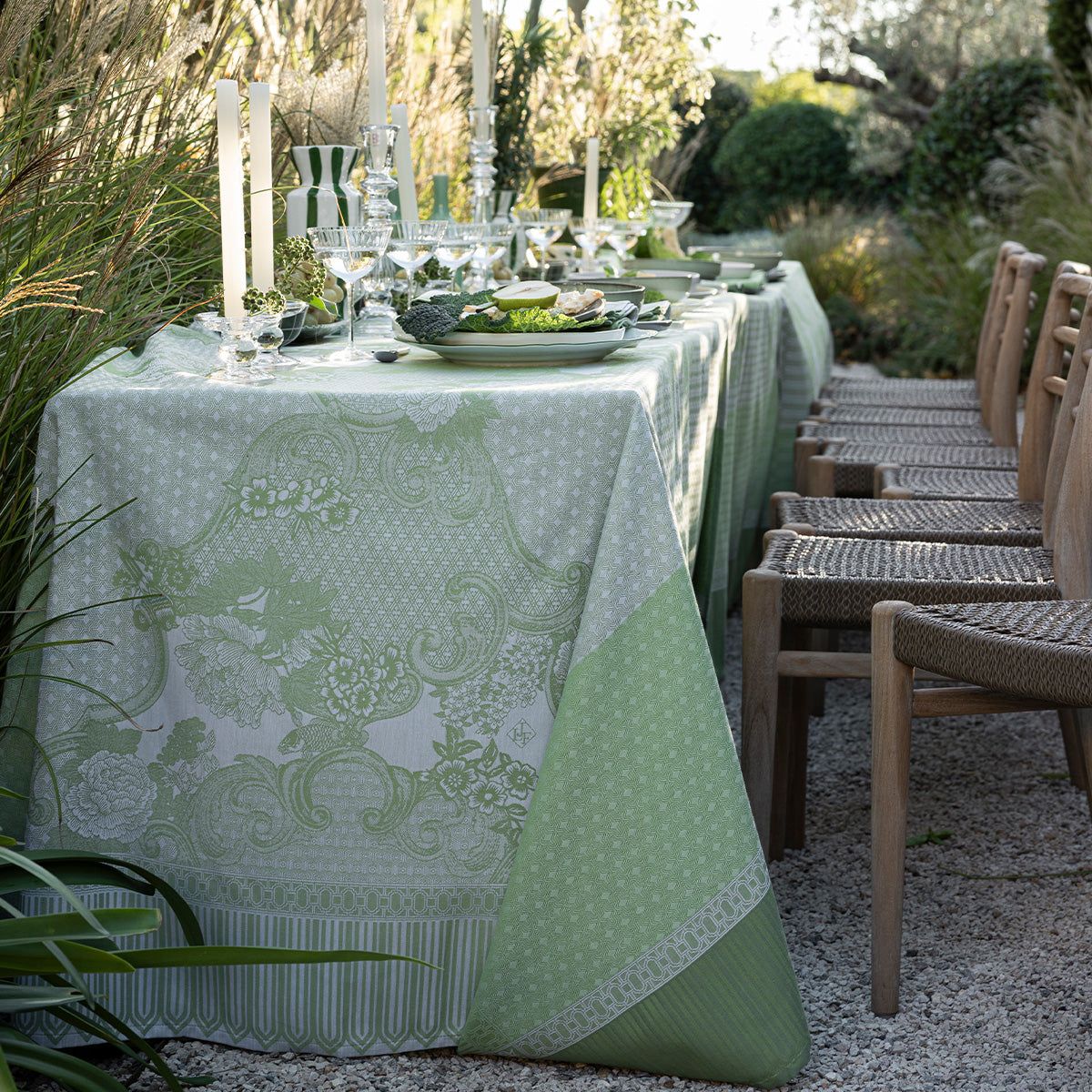 Outdoor dining setup with a patterned green tablecloth and chairs in a garden setting.
