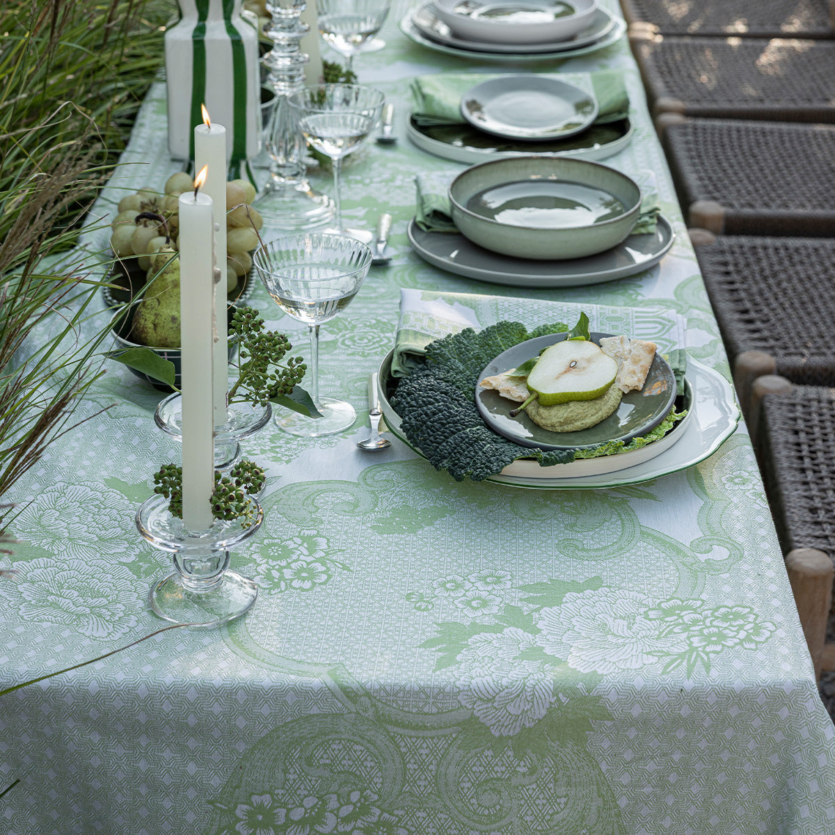 Elegant outdoor dining table setting with green and white tablecloth, plates, and candles.
