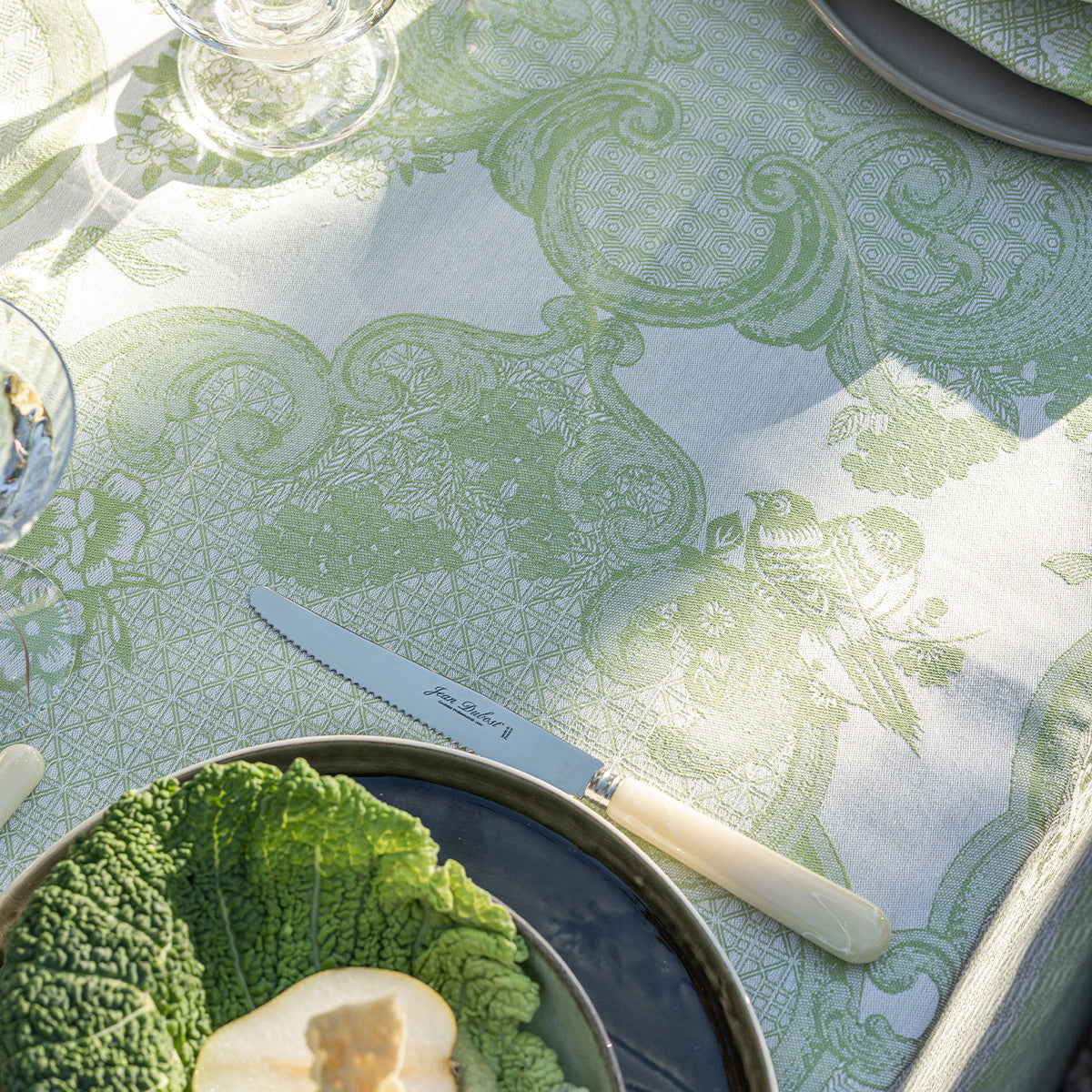 Table setting with green patterned tablecloth, plates, and cutlery.