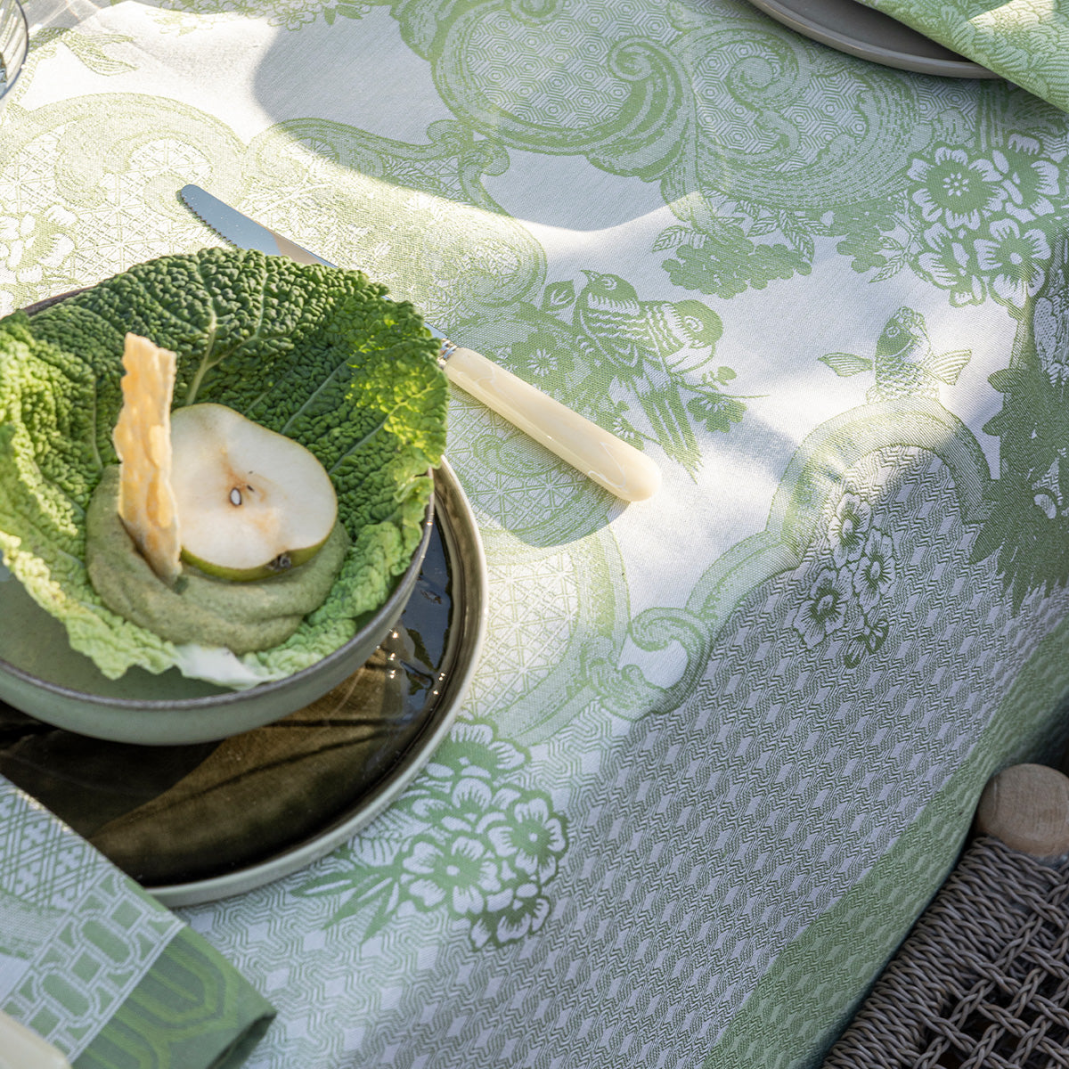 Green and white patterned tablecloth with a bowl of fruit on a table.