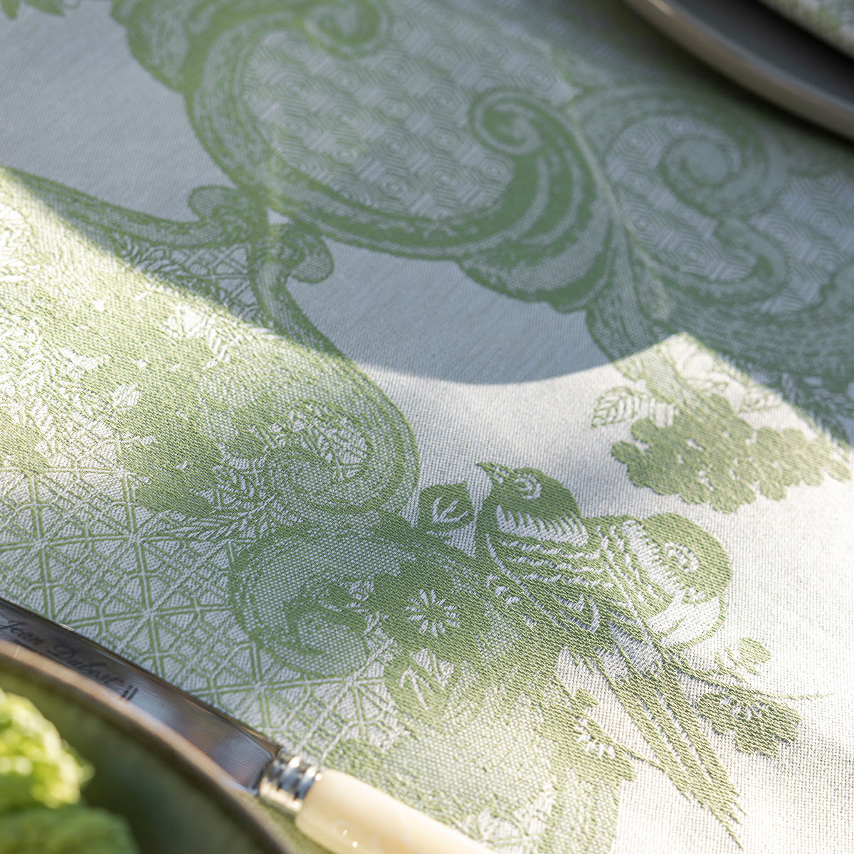 Close-up of a green patterned tablecloth with a knife and plate on a table.