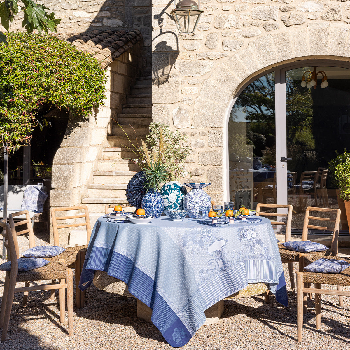 Outdoor dining setup with a tablecloth, chairs, and decorative items in front of a stone building.
