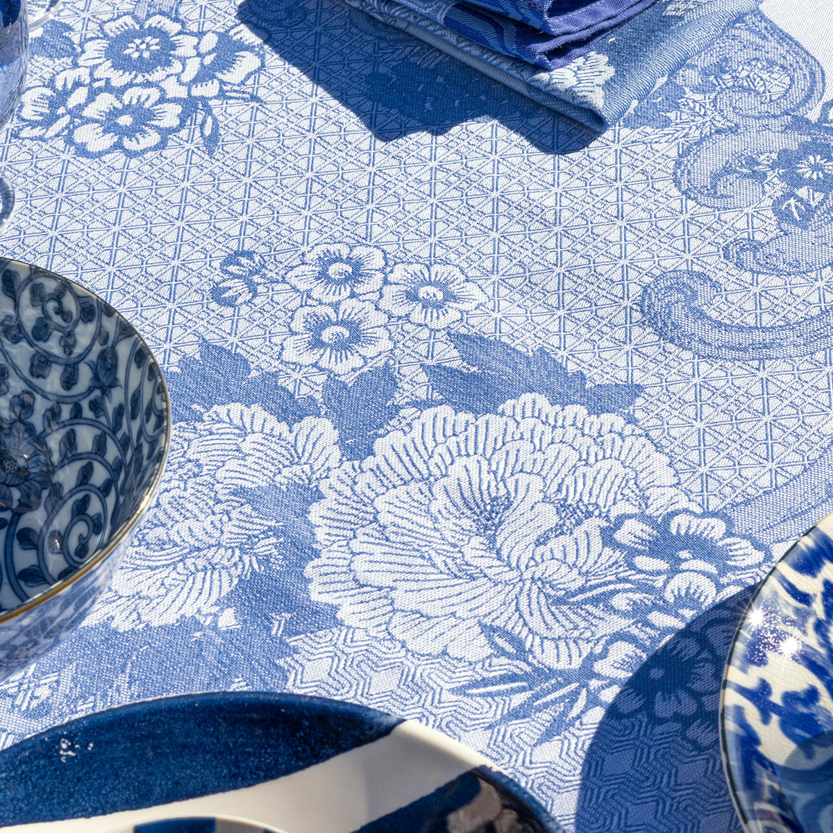 Blue and white patterned coated tablecloth with floral and geometric designs, accompanied by blue and white ceramic plates and bowls.