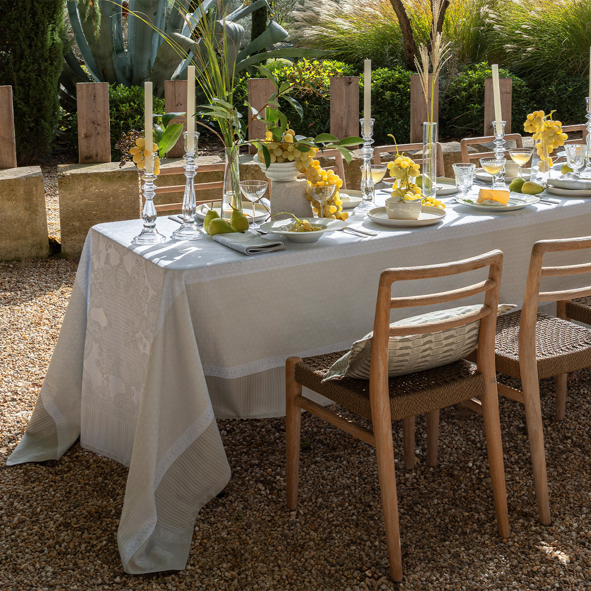 Elegant outdoor dining table setting with white coated tablecloth, candles, and yellow flowers.