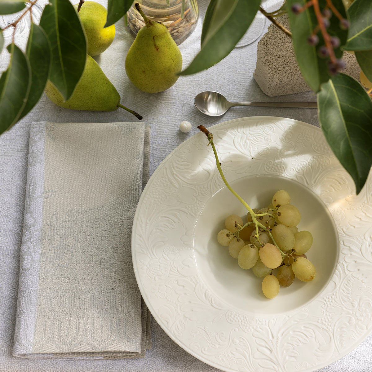 Table setting with a white plate, grapes, pears, and a napkin on a light surface.