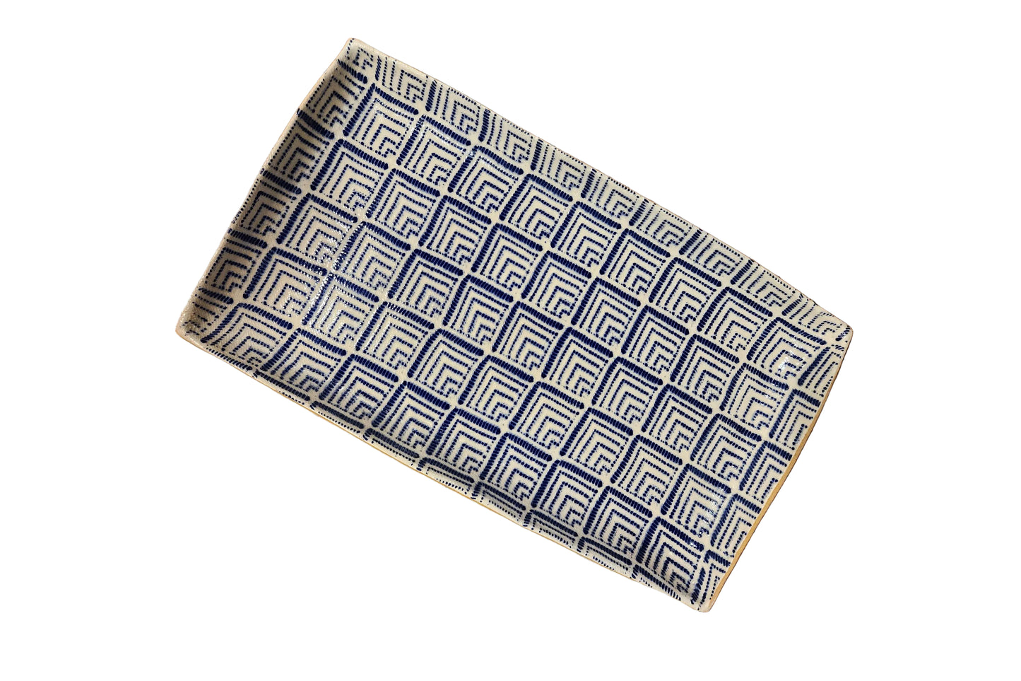 A rectangular woven tray with a geometric Greek key pattern in navy blue and cream, shown on a rustic wooden plank floor.