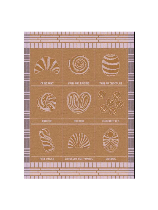 A towel featuring nine illustrated French pastries arranged in a tan background, with a lavender and beige patterned border. The illustrations are rendered in a light cream or off-white tone, with the names of the pastries printed below each drawing.