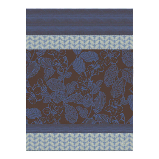 A close-up of a fabric or wallpaper pattern featuring a dark brown background with a blue floral vine design, bordered by blue striped and light blue chevron bands.